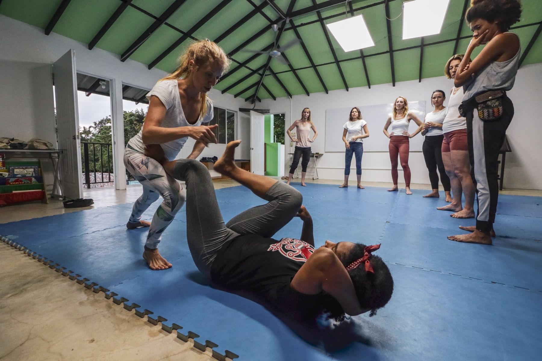 An instructor demonstrating a jiu-jitsu technique on a mat while a group of women watches.