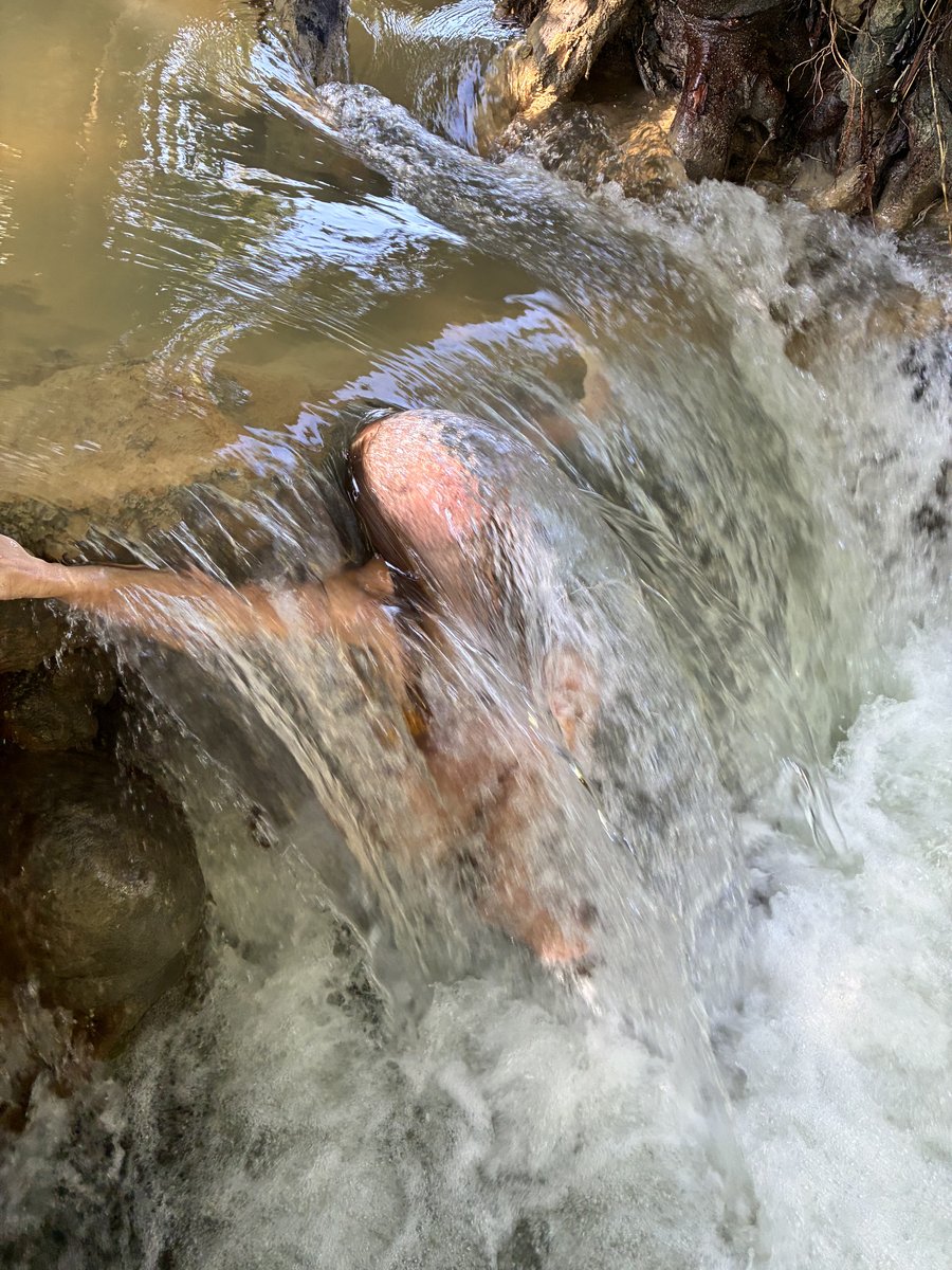 A swimmer partly visible beneath a rush of river water pouring over rocks.