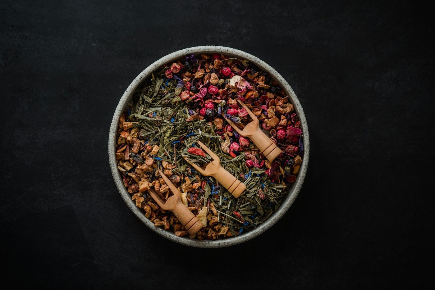 Un cuenco con una mezcla de hierbas y frutas secas a granel para infusión, con dos cucharas de madera.
